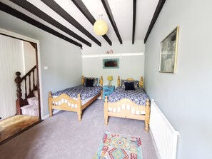 A room with two wooden beds, a patterned rug, a ceiling with exposed beams, and a hanging light fixture.