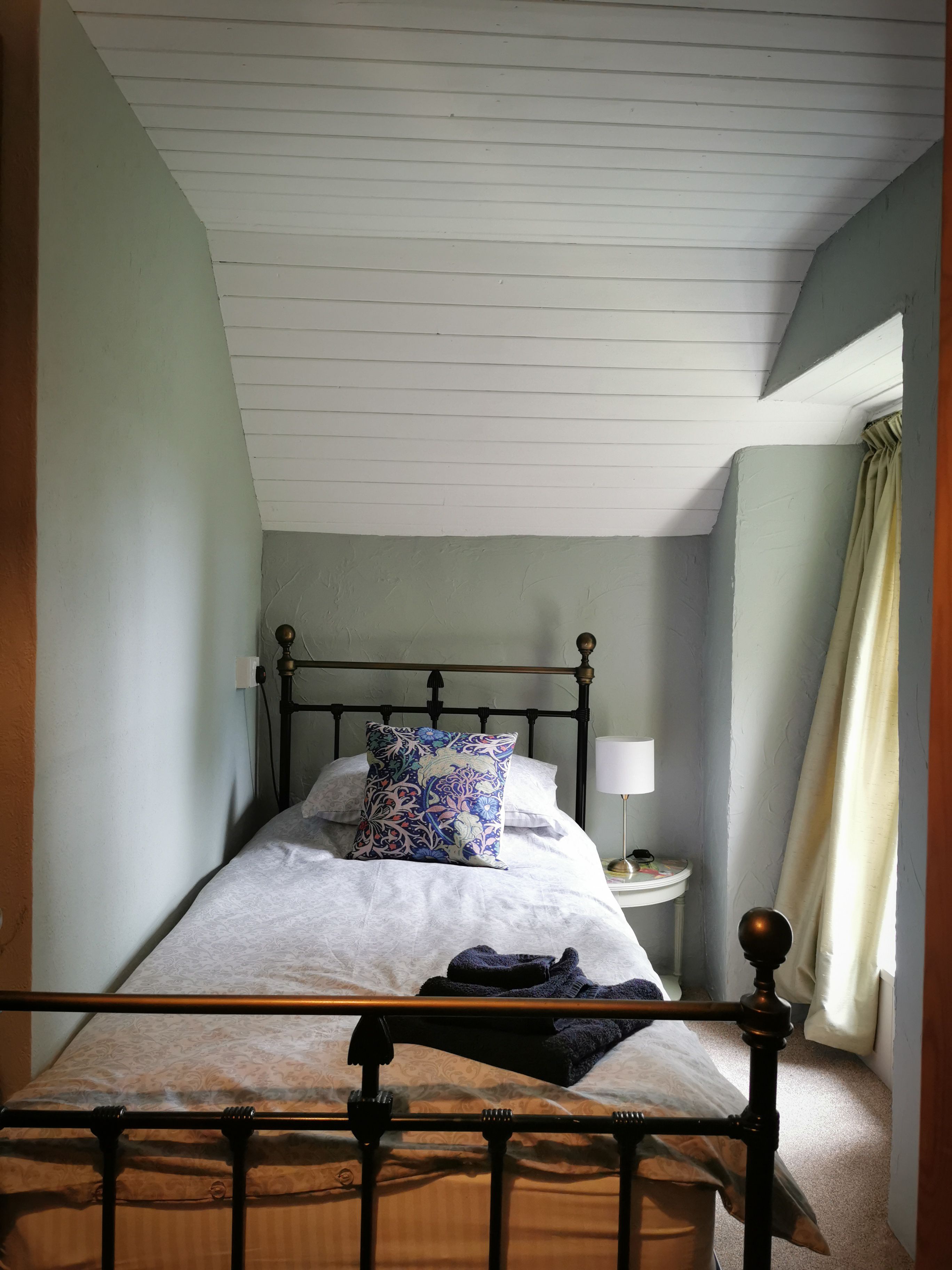 Un dormitorio con cama, mesita de noche, lámpara y ventana con cortinas.
