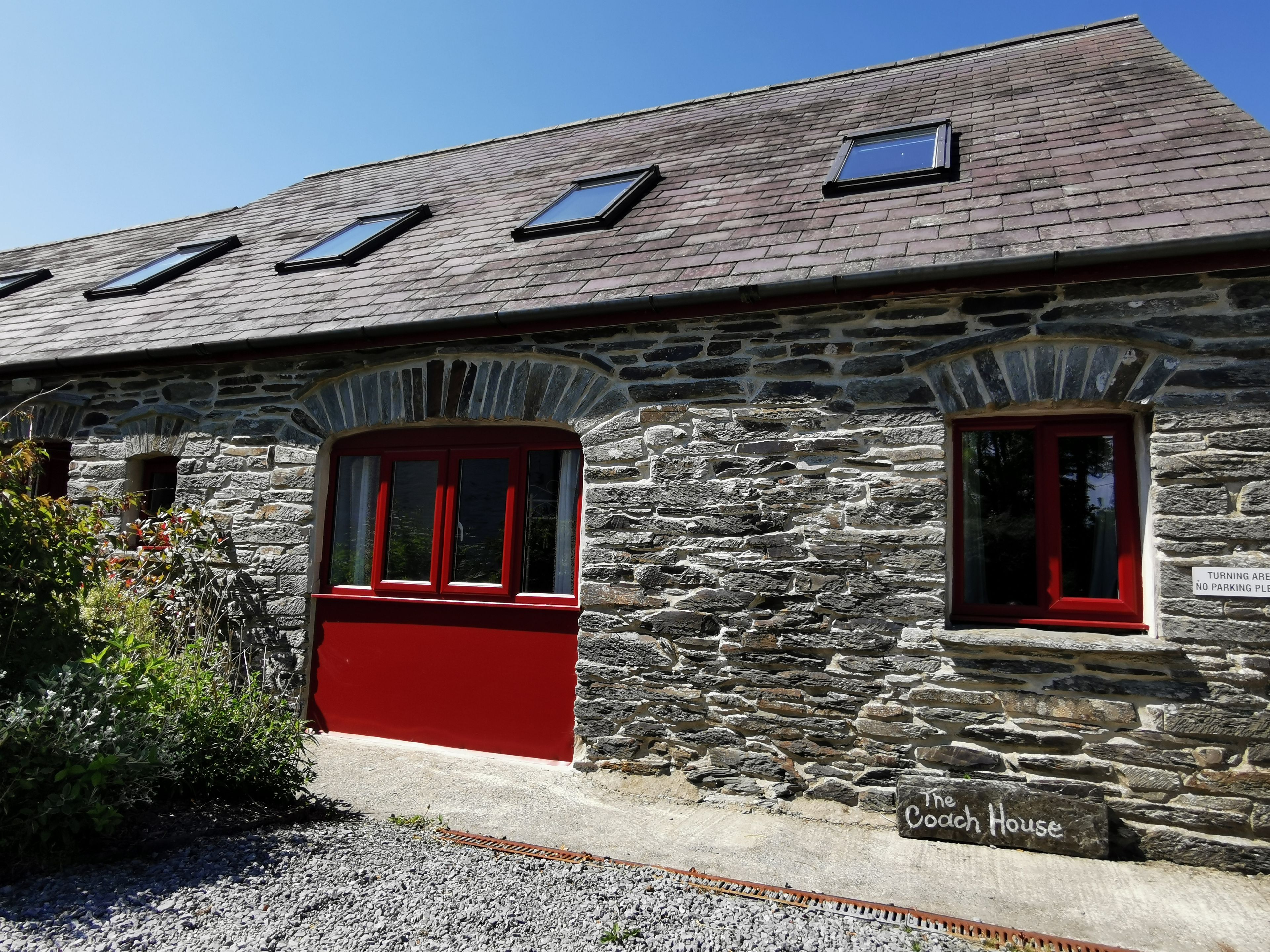 Edificio de piedra con puerta roja y ventanas, identificado como 'The Coach House'.