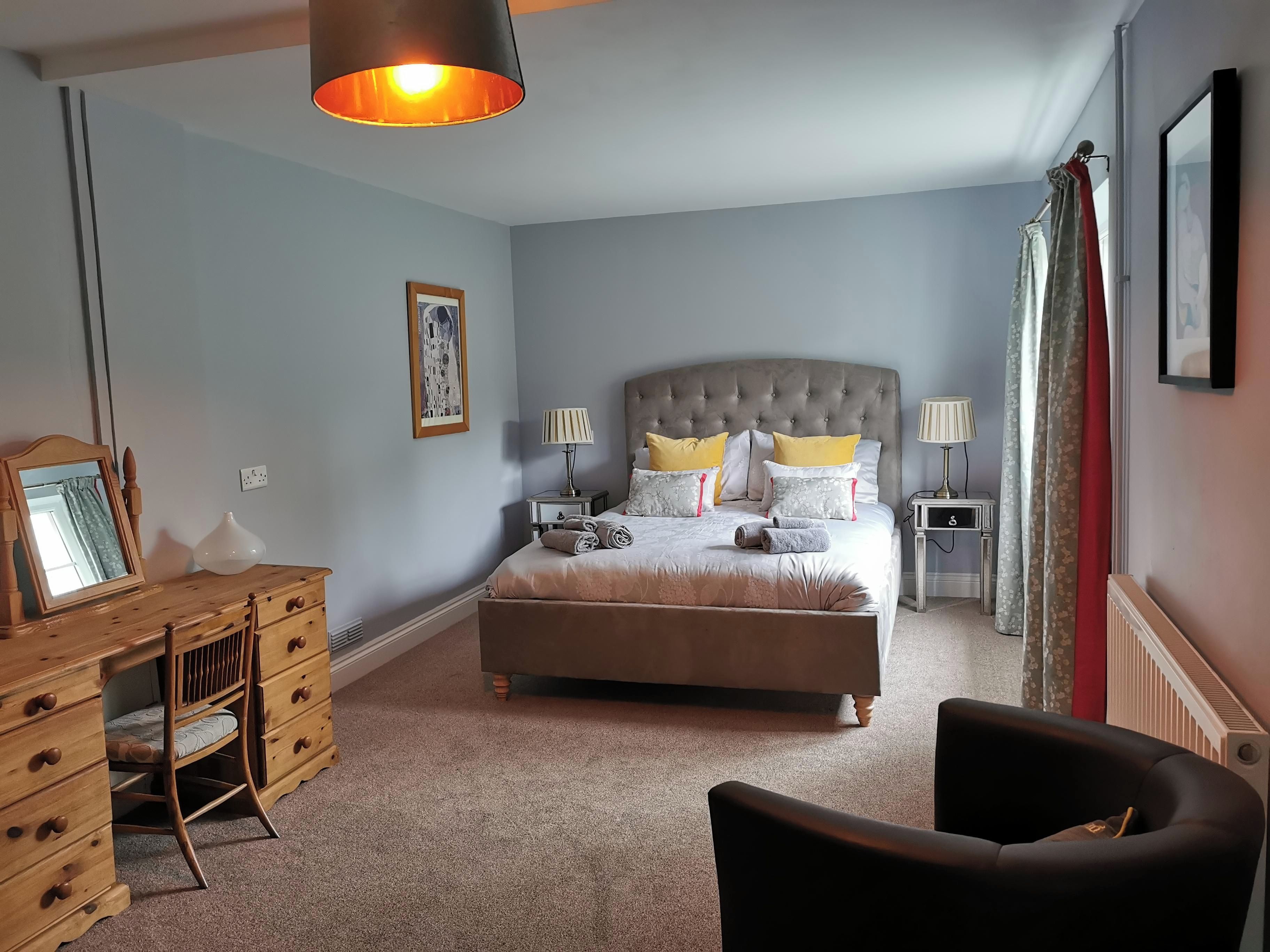Ein Schlafzimmer mit einem Bett, Nachttischen, einem Schreibtisch, einem Sessel und einer Pendelleuchte.