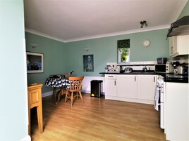 Una cocina con armarios blancos, una mesa de comedor de madera y una encimera negra.