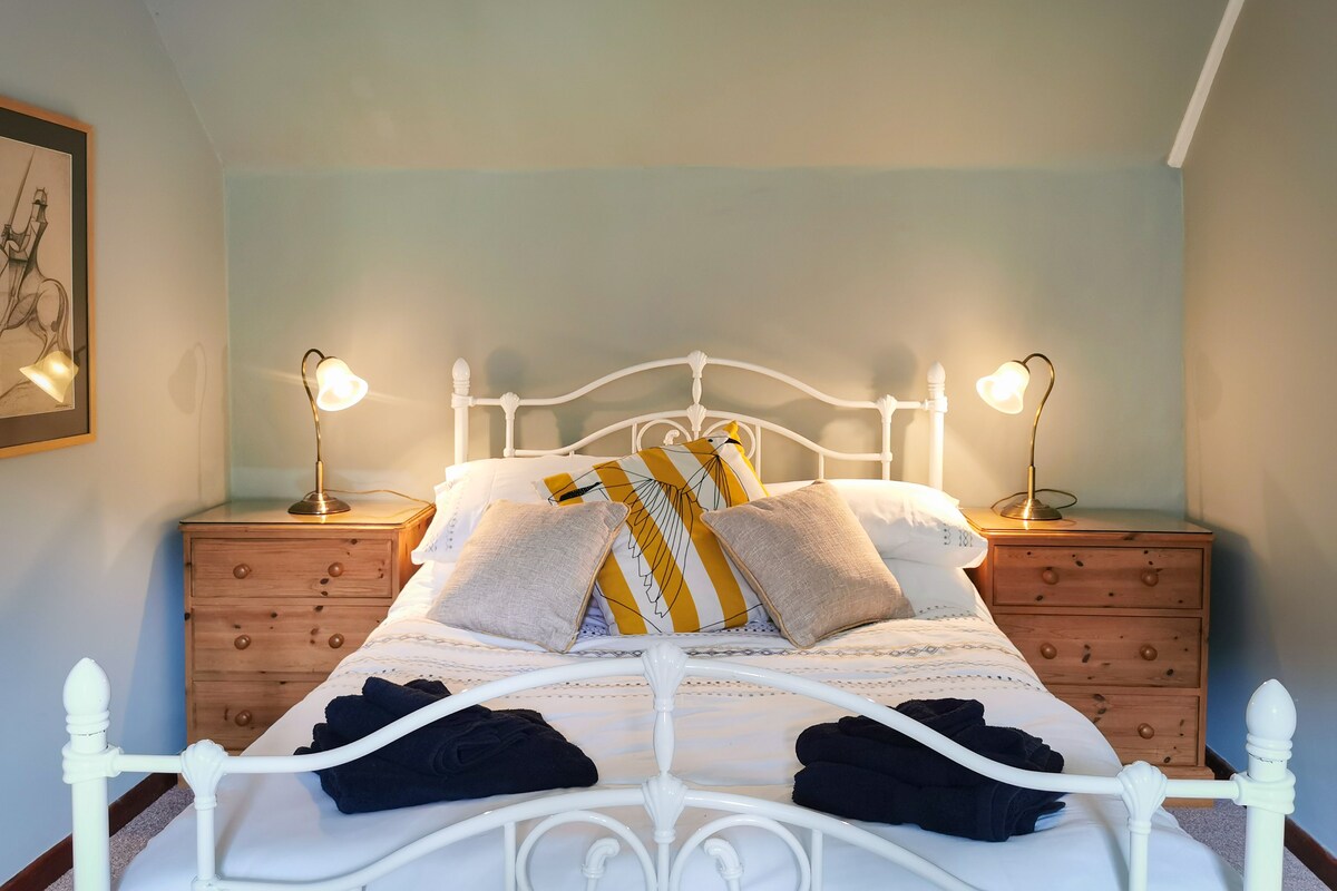 Ein ordentlich gemachtes Bett mit weißer Bettwäsche und mehreren Kissen, an beiden Seiten mit Nachttischen und Lampen.