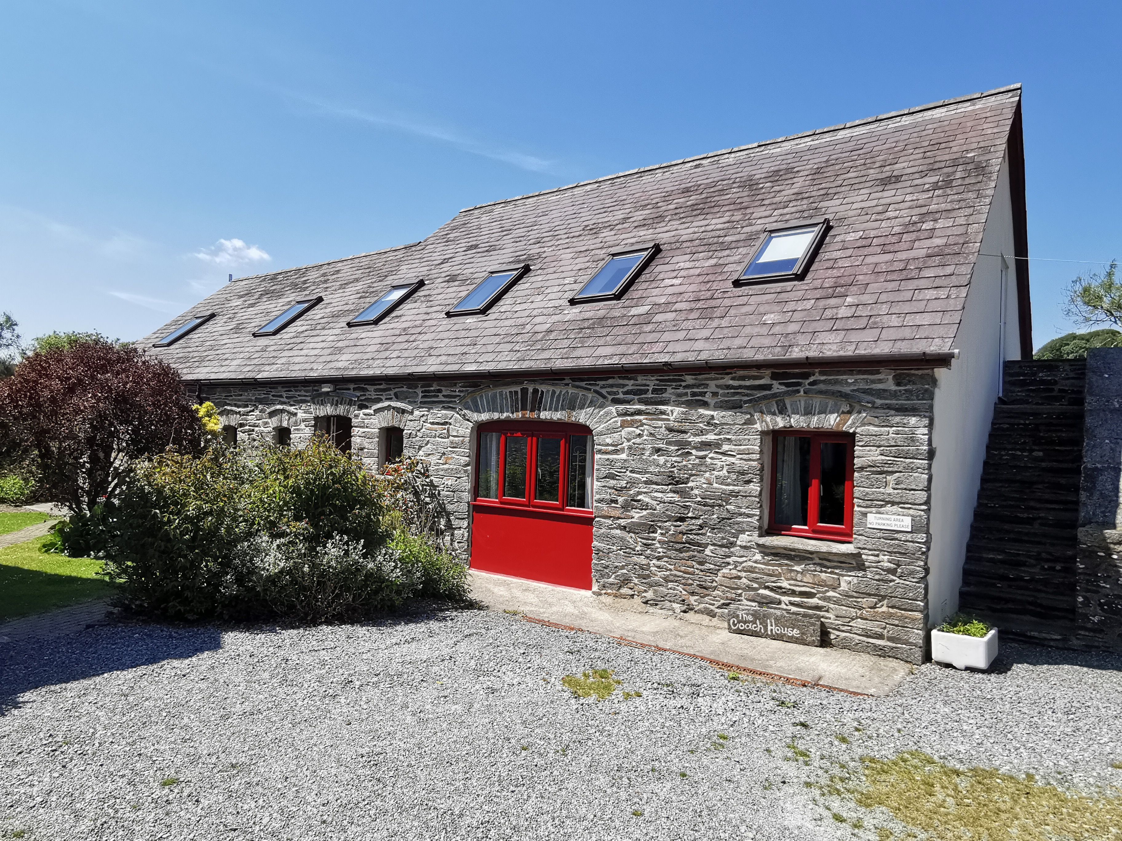 Un edificio de piedra con puerta roja y varias ventanas, identificado como "The Coach House".