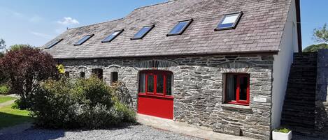 Un edificio de piedra con puerta roja y varias ventanas, identificado como "The Coach House".