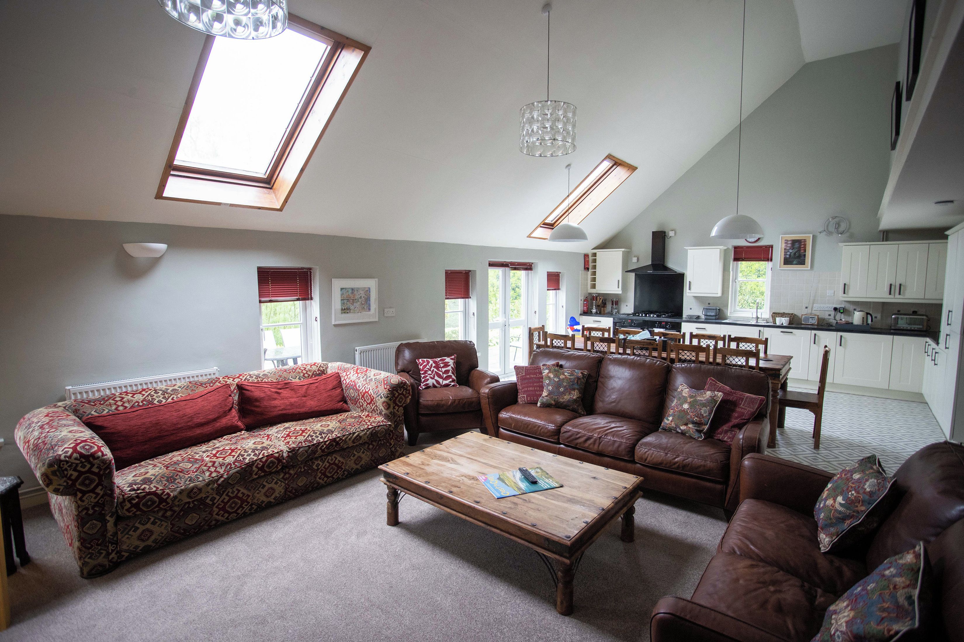 A spacious living room with a large sofa, a coffee table, and a dining area with a kitchen in the background.