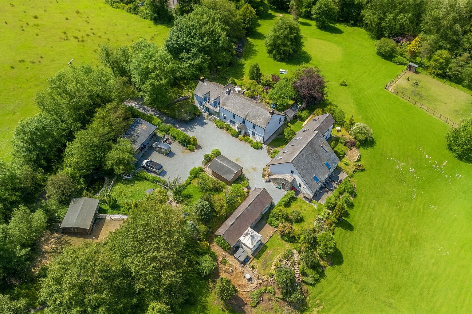 An aerial view of a property with multiple buildings, a parking area, and surrounding green fields.