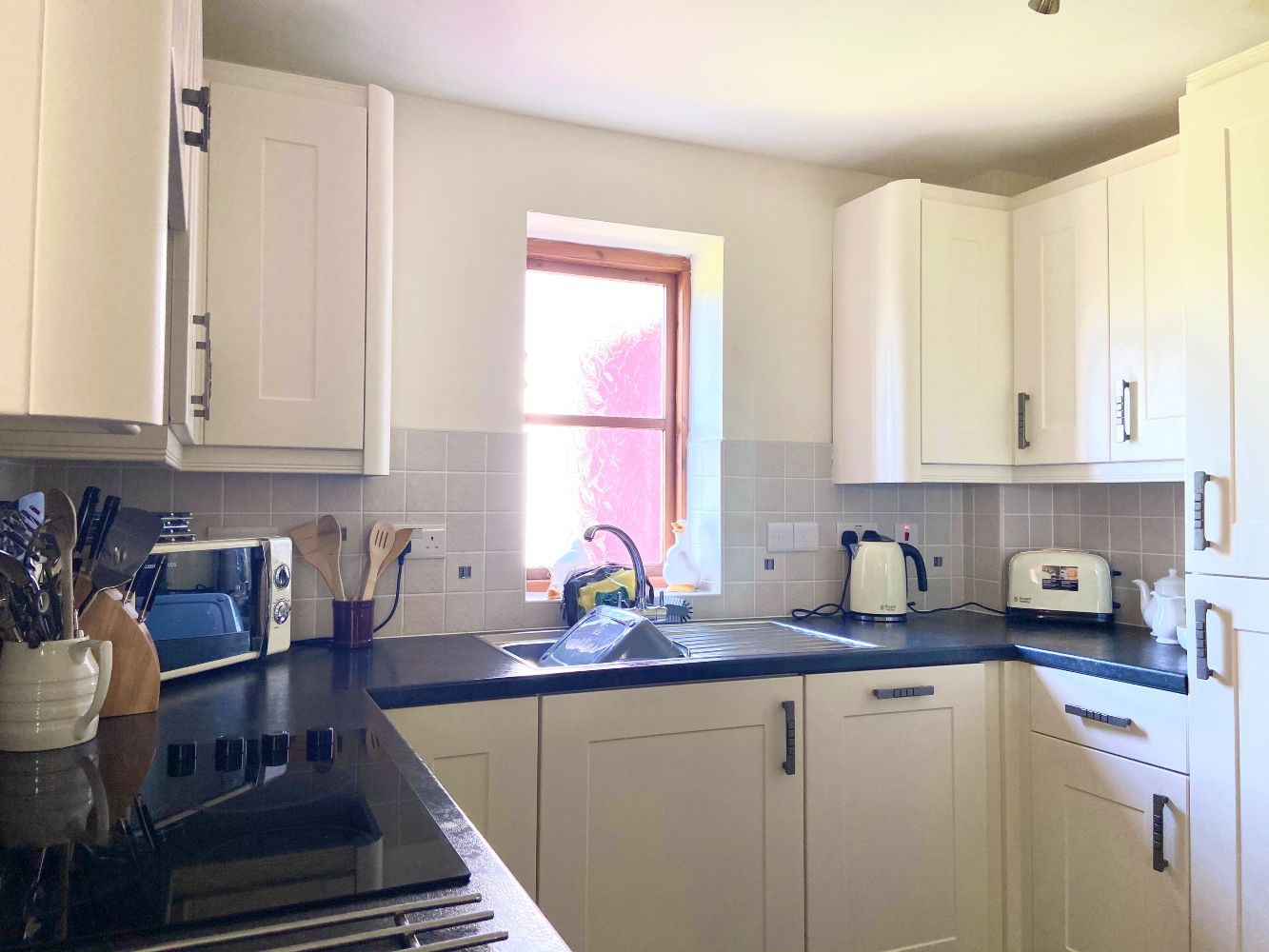 A kitchen with white cabinets, a black countertop, a window, and a toaster.