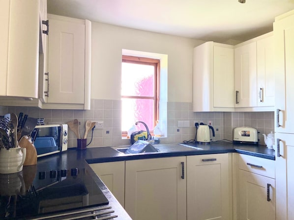 A kitchen with white cabinets, a black countertop, a window, and a toaster. - Wellstone Cottages  (Llanfyrnach)