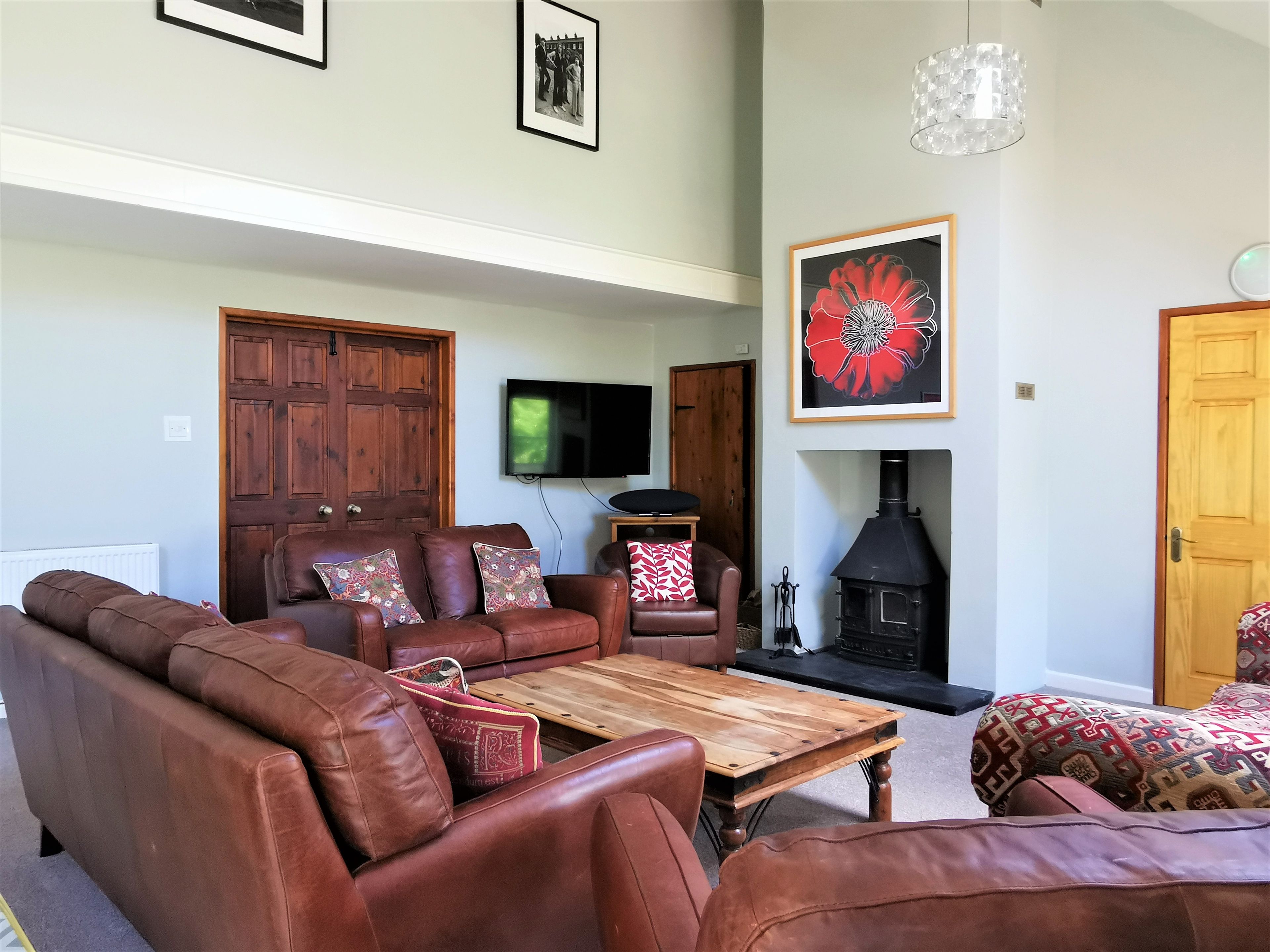 Una sala de estar con un sofá de cuero marrón, una mesa de centro de madera, una chimenea y un televisor montado en la pared.
