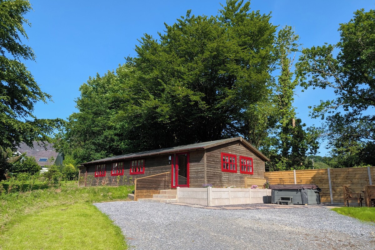 Une cabane en bois avec une allée de gravier, entourée d’arbres et sous un ciel dégagé.