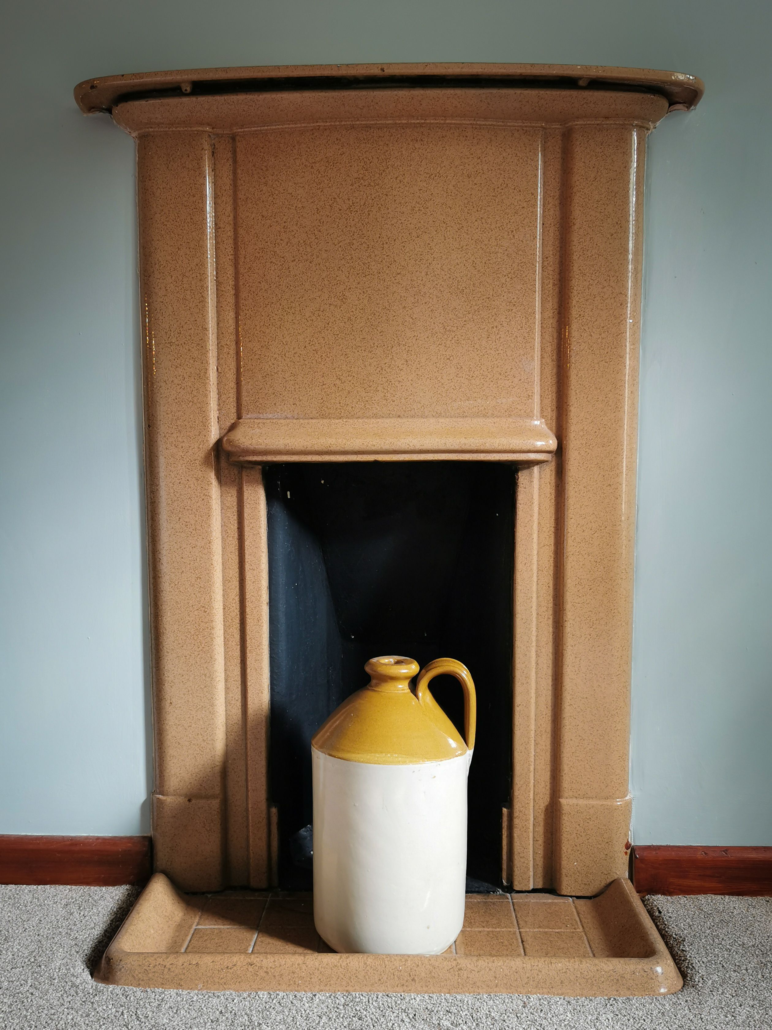 Una chimenea con un gran jarro blanco y amarillo colocado frente a ella.