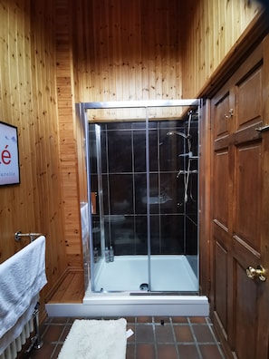 Ein Badezimmer mit Holzwandverkleidung, einer gläsernen Duschkabine, einem weißen Handtuch und einem gefliesten Boden.