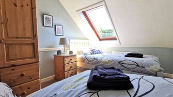 A bedroom with two beds, a wooden wardrobe, a nightstand, and a window with a view of greenery.
