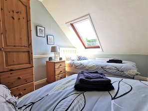 A bedroom with two beds, a wooden wardrobe, a nightstand, and a window with a view of greenery. - Wellstone Cottages  (Llanfyrnach)