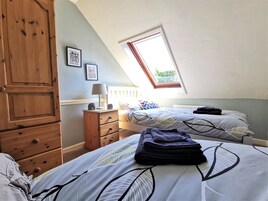 Un dormitorio con dos camas, un armario de madera, una mesita de noche y una ventana con vistas a la vegetación.