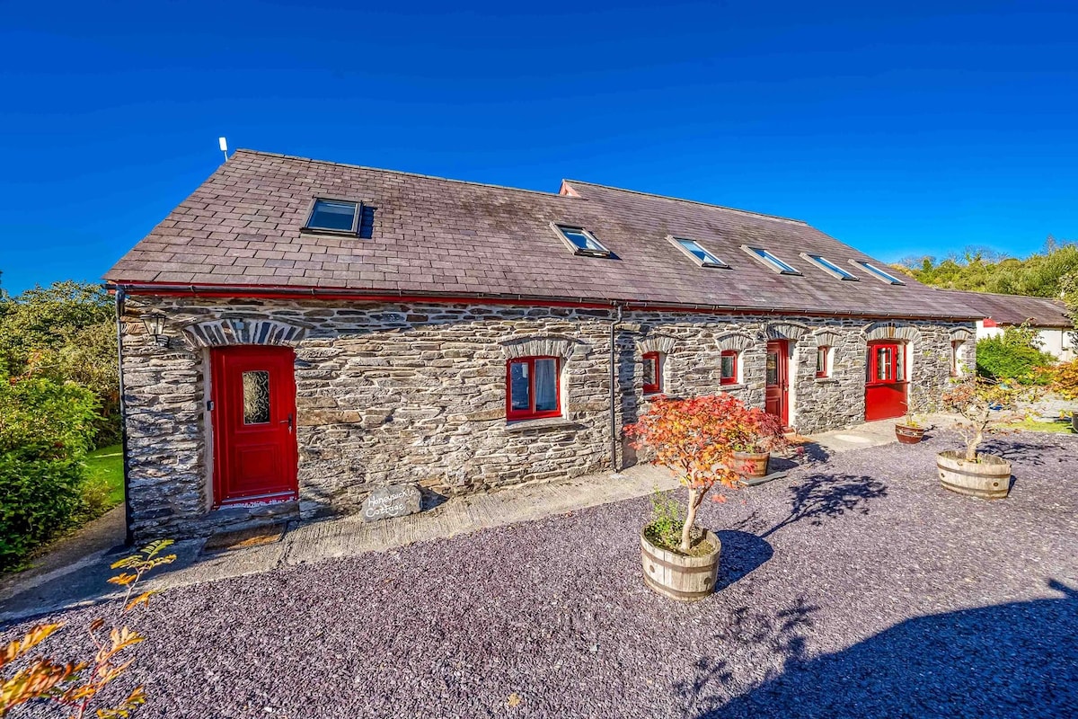 A stone cottage with a red door, multiple windows, and a gravel driveway.