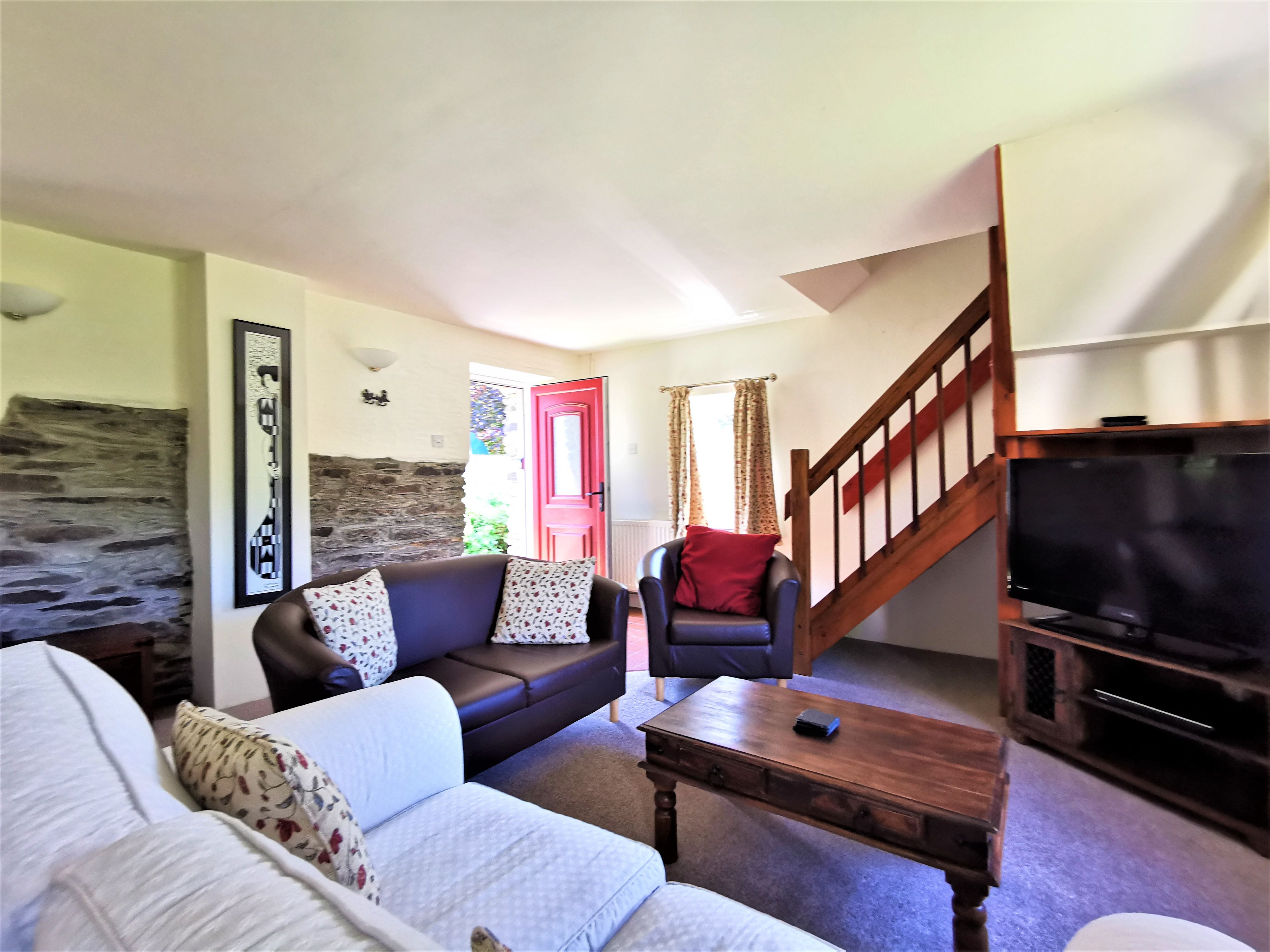 Una sala de estar con un sofá, una mesa de centro, un televisor y una escalera que conduce a otra habitación.
