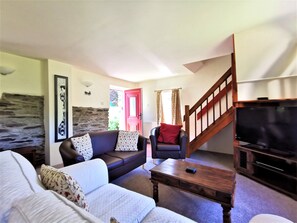 Una sala de estar con un sofá, una mesa de centro, un televisor y una escalera que conduce a otra habitación.