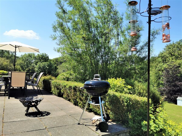 Un patio al aire libre con una parrilla, una mesa con sillas y una lámpara colgante.