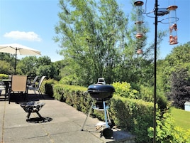 Un patio al aire libre con una parrilla, una mesa con sillas y una lámpara colgante.