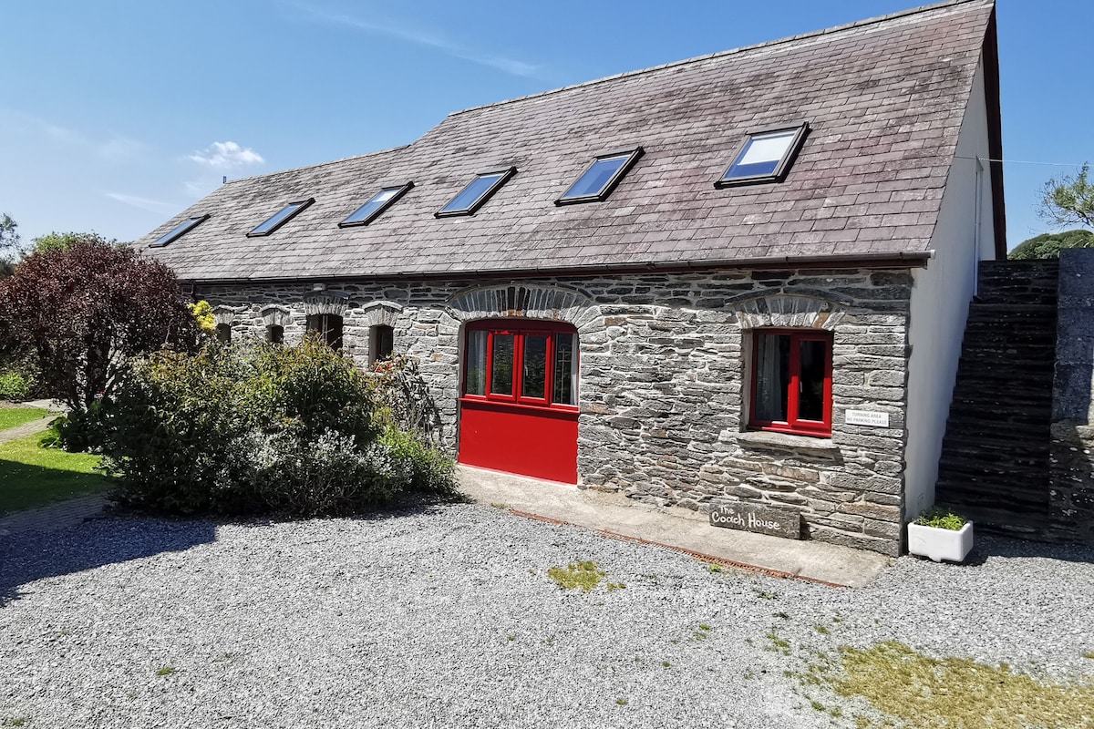A stone building with a red door and multiple windows, labeled "The Coach House."