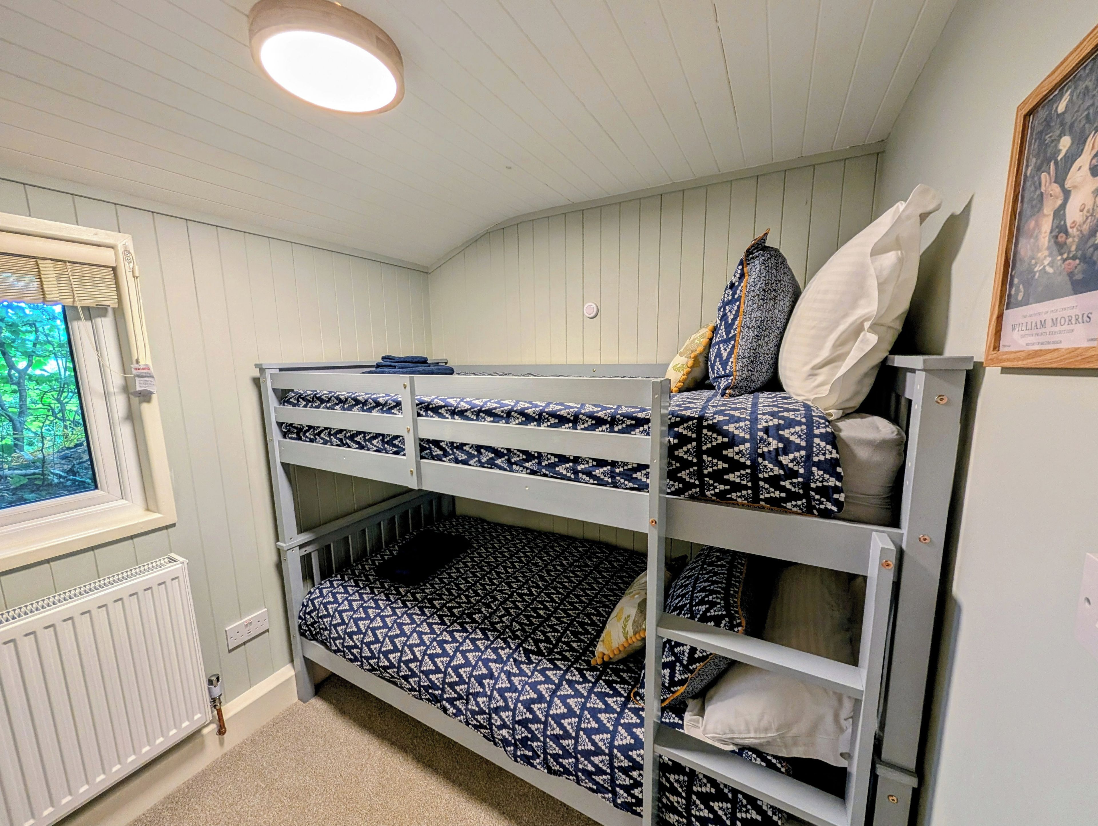 Et værelse med køjeseng, et vindue, en radiator og et billede i ramme på væggen.