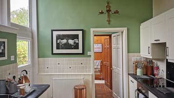 A kitchen with a tiled backsplash, a framed picture of sheep, a copper kettle, and a door leading to a hallway.