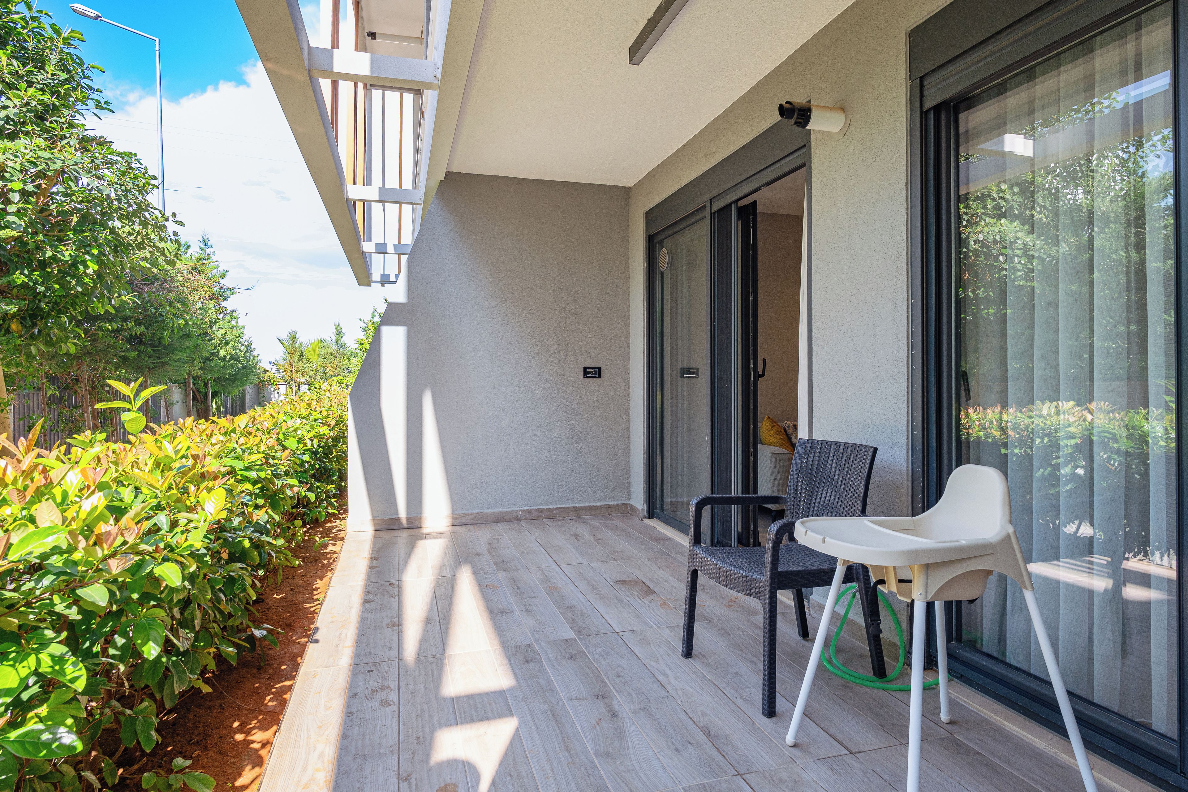 A balcony with a chair, a small table, and a view of greenery and a building.