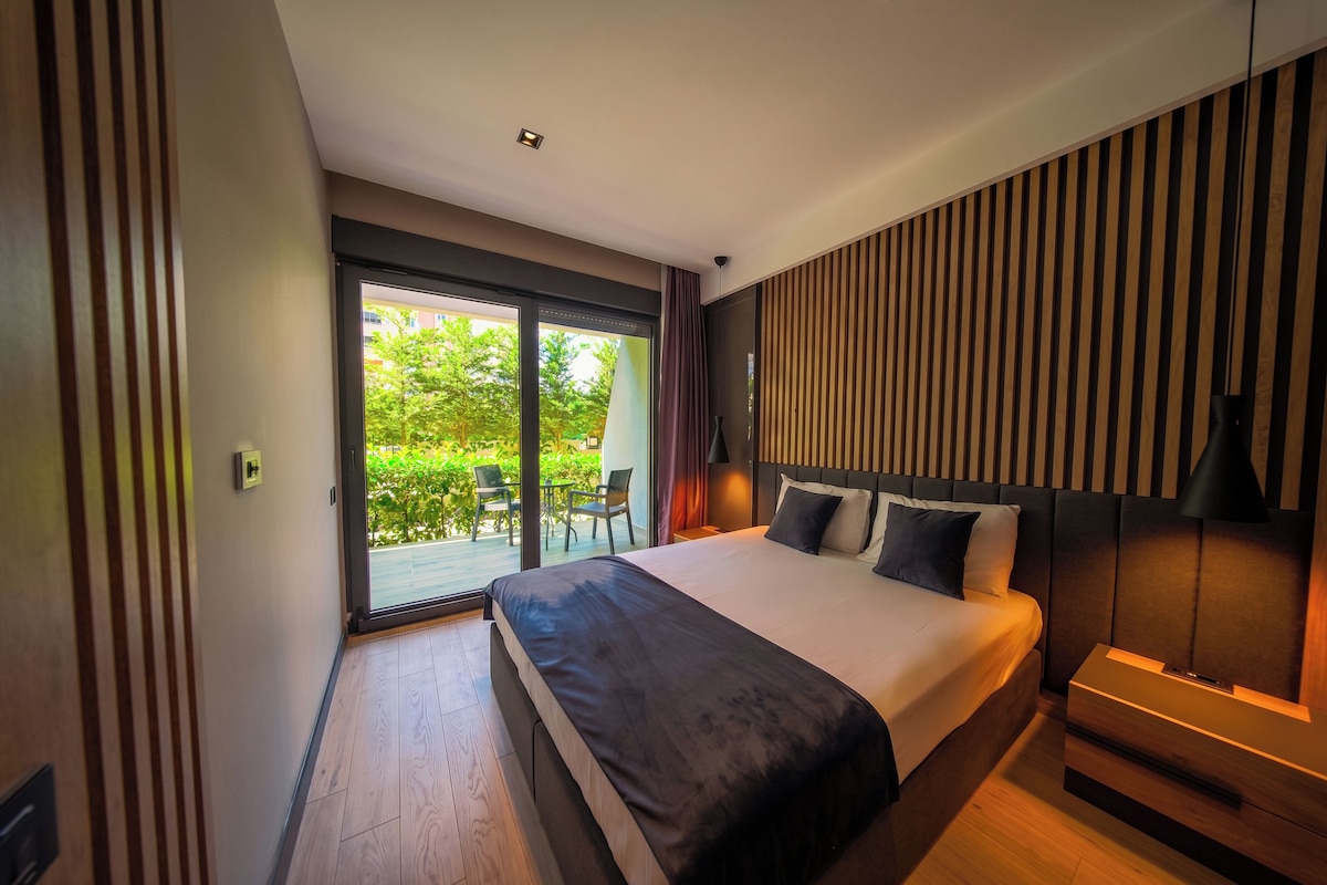 A modern hotel room with a large bed, a sliding glass door to a balcony, and a wooden slatted wall design.