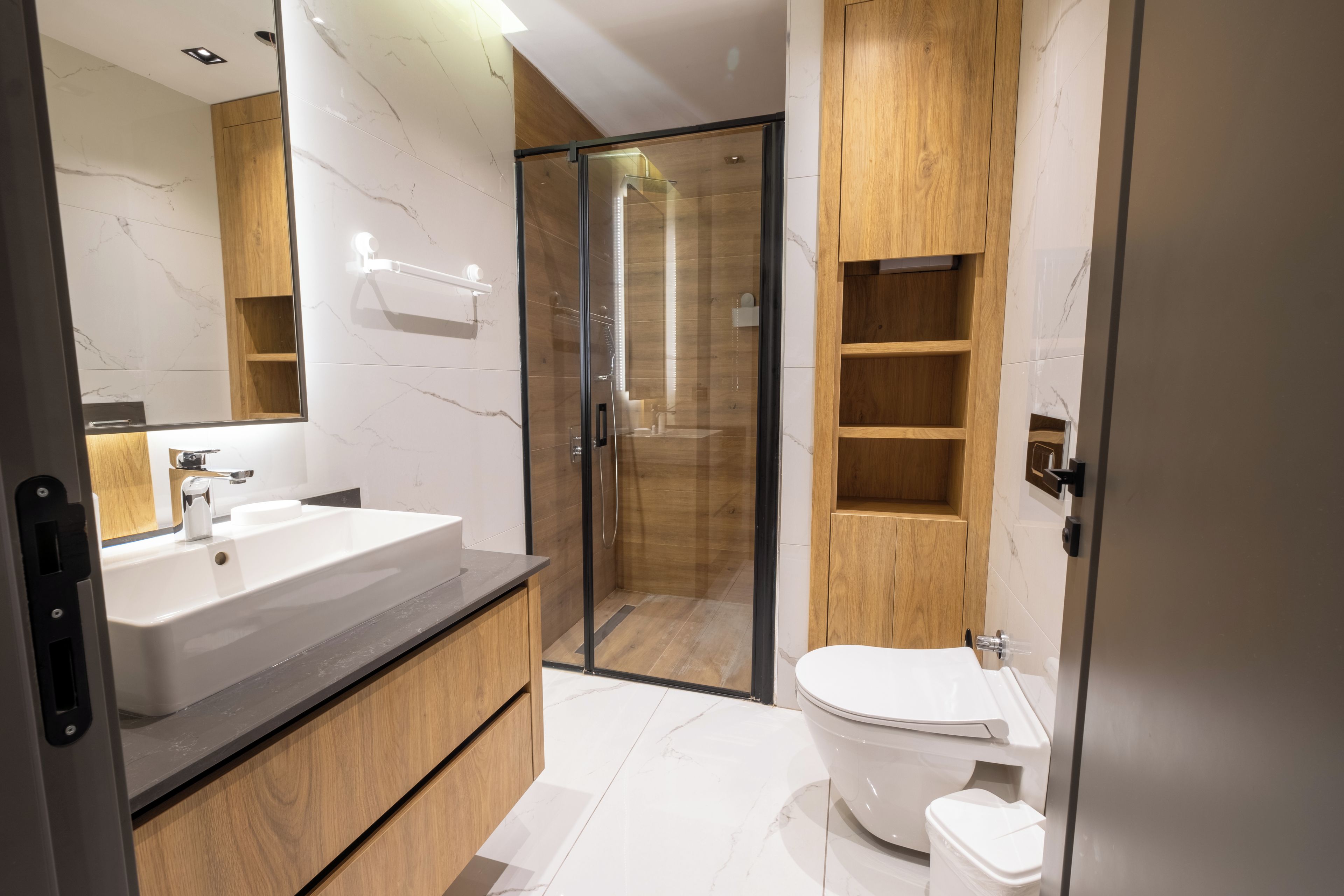 Un baño moderno con ducha de vidrio, un lavamanos grande y estantes de madera.