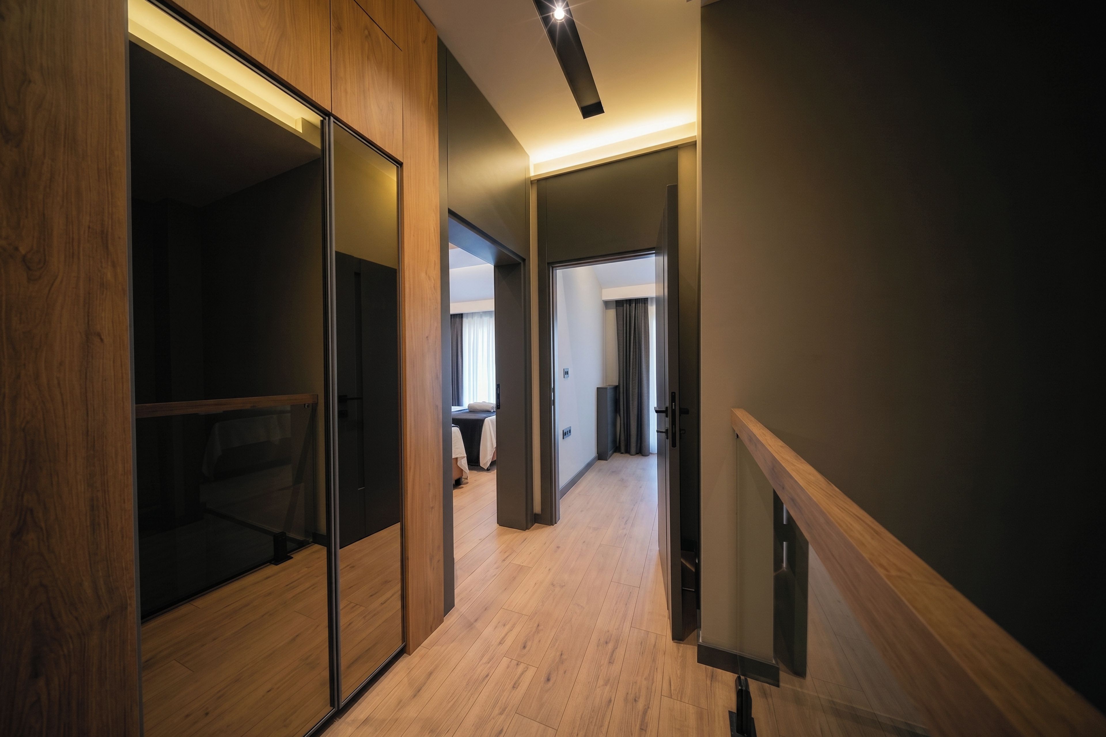A modern hotel corridor with wooden flooring, glass partitions, and a neutral color scheme.