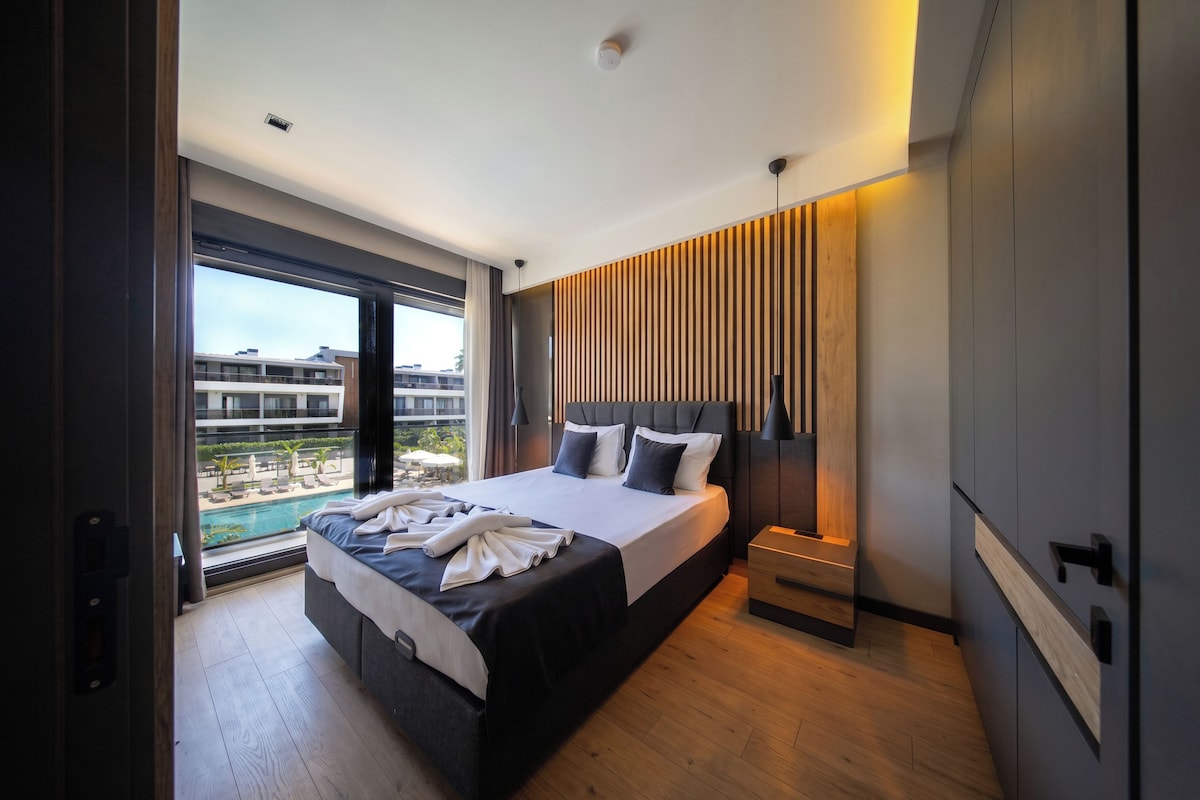 A modern hotel room with a large bed, a view of a pool, and a cityscape.