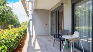 A balcony with a chair, a small table, and a view of greenery and a building.