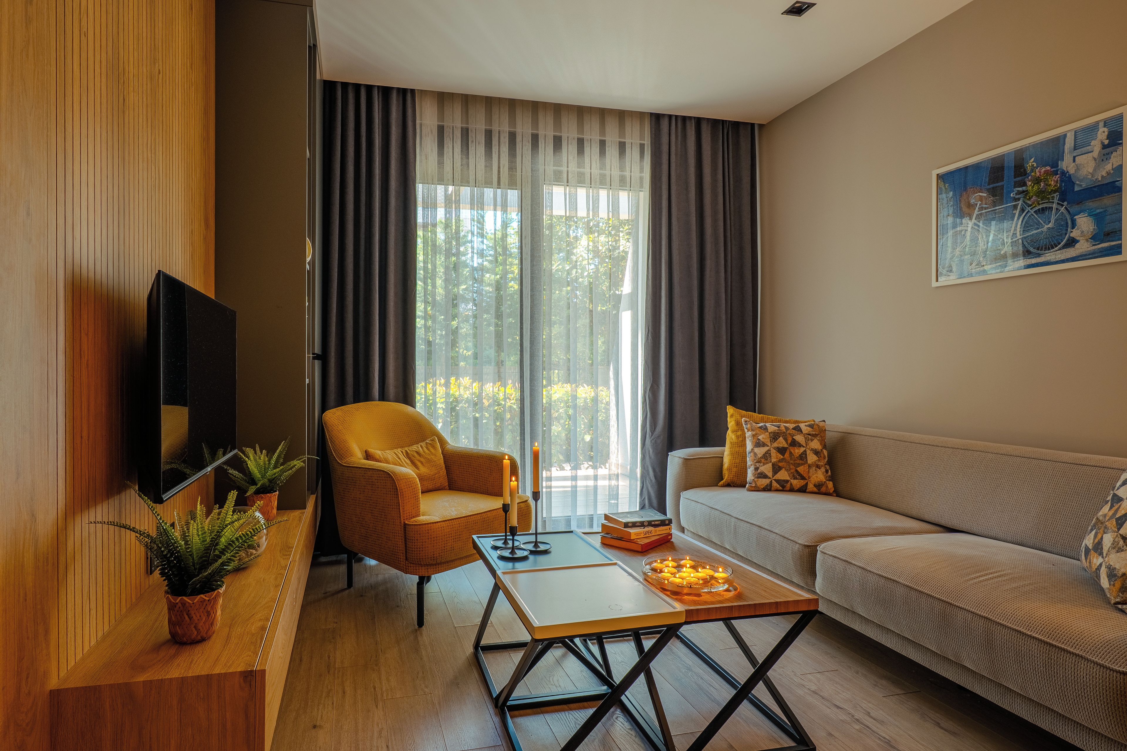 A modern living room with a sofa, armchair, coffee table, and a flat-screen TV mounted on a wooden wall.
