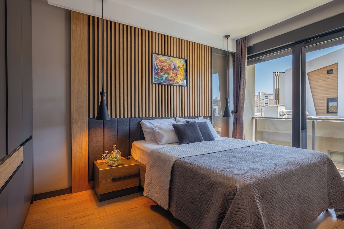 A modern bedroom with a bed, nightstand, and a large window.