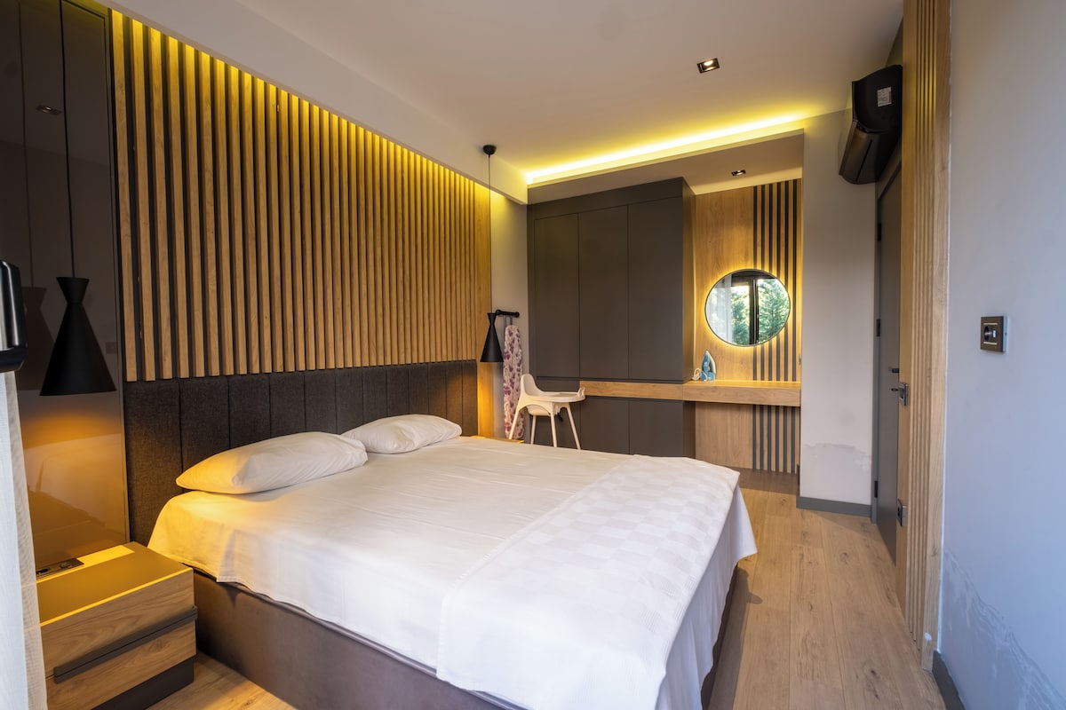 A modern bedroom with a bed, bedside tables, a mirror, and a wardrobe.