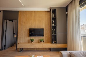 A modern living room with a wooden panel wall, a flat-screen TV, a bench with potted plants, and a grey shelving unit.