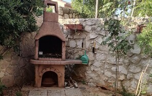 A stone-built outdoor oven with a chimney, surrounded by a stone wall and greenery. - 1 bedroom stunning apartment in Cres (Cres)