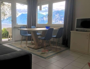 Ein Essbereich mit Tisch und Stühlen, einem Fernseher auf einem Schrank und Blick auf Berge durch große Fenster.
