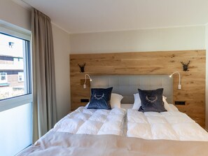 Ein Doppelbett mit Holz Kopfteil, zwei Wandleuchten zum Lesen und ein Fenster mit Vorhängen.