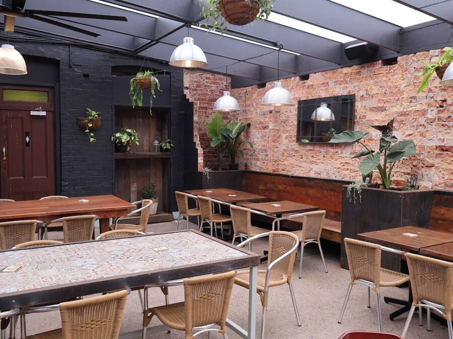 Interior de restaurante con paredes de ladrillo, plantas colgantes y una combinación de muebles de madera y metal.