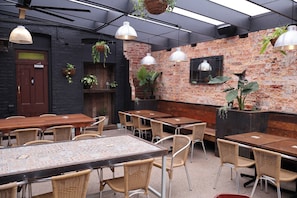 A restaurant interior with brick walls, hanging plants, and a mix of wooden and metal furniture.