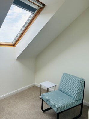 Ein Zimmer mit schrägem Dach, einem Oberlicht, einem einzelnen Sessel und einem kleinen Tisch.