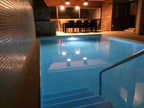 An indoor swimming pool with a glass barrier, steps leading into the pool, and a seating area with tables and chairs in the background. - Villa in Pula With Swimming Pool (Pula)