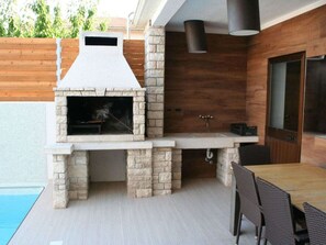 An outdoor kitchen with a stone chimney, a built-in grill, and a dining area with chairs. - Villa in Pula With Swimming Pool (Pula)
