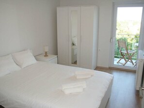 A bedroom with a large bed, a wardrobe, a nightstand with a lamp, and a balcony with a chair. - Villa in Pula With Swimming Pool (Pula)