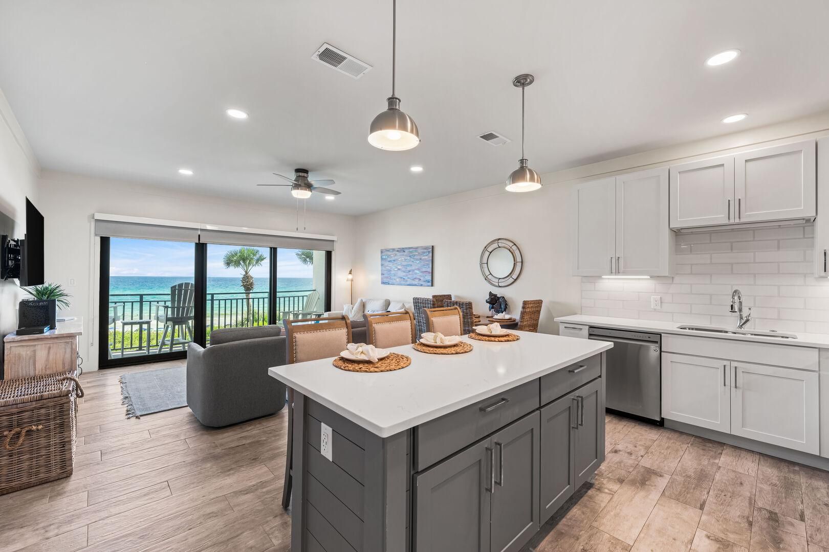 A modern kitchen with a large island, white cabinets, and a view to the ocean.