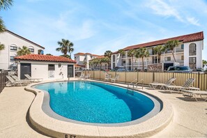 Ein Pool mit Liegestühlen und einem umzäunten Bereich, umgeben von Gebäuden mit roten Ziegeldächern.