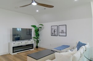 Una sala de estar moderna con un televisor de pantalla plana, un ventilador de techo, una planta grande y dos cuadros en la pared.