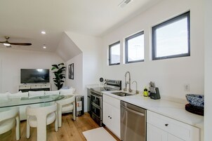 Una cocina moderna con comedor, que incluye una mesa de vidrio, sillas blancas, horno empotrado y pileta de acero inoxidable.